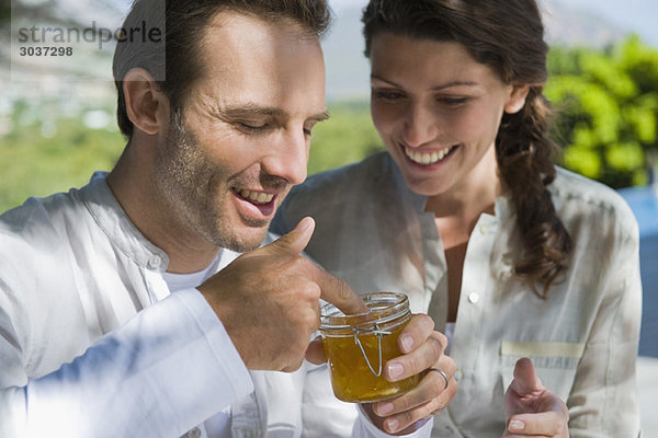 Mann hält ein Glas Marmelade mit einer Frau  die neben ihm lächelt.