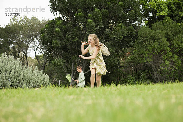 Mädchen und Junge spielen mit Schmetterlingsnetzen im Garten