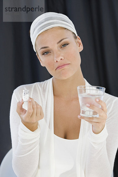 Frau  die eine Flasche Medizin mit einem Glas Wasser hält