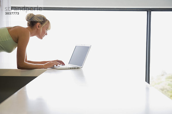 Frau stützt sich auf eine Theke und arbeitet an einem Laptop