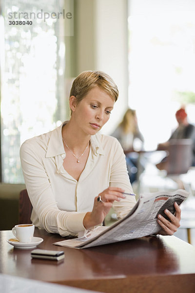 Geschäftsfrau sitzt in einem Restaurant und liest eine Finanzzeitung.