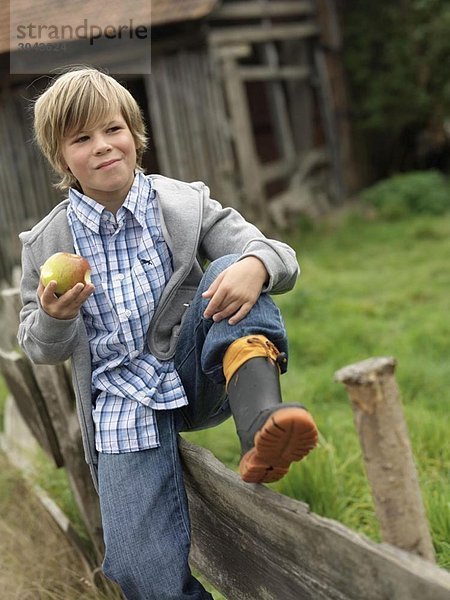 Junge isst Apfel  sitzt auf dem Zaun