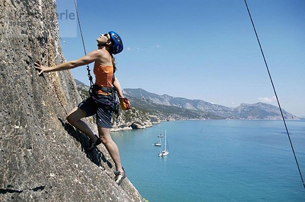 Frau beim Felsklettern  Bucht im Hintergrund