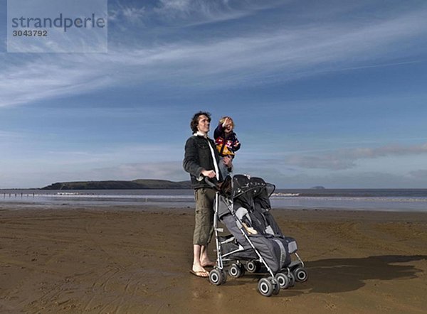 Mann am Strand mit Kinderwagen und Kind