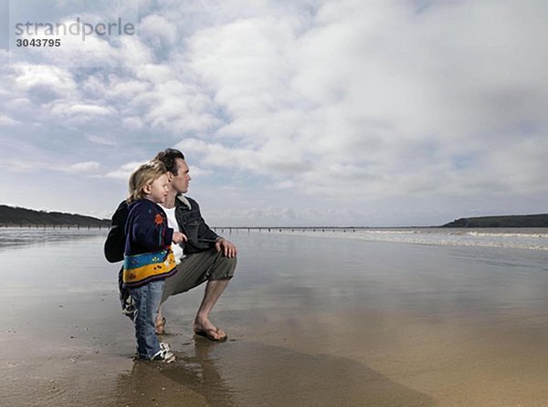 Mann und Kind mit Blick aufs Meer am Strand