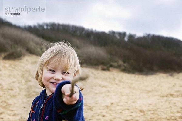 Junge am Strand  der mit dem Stock zeigt