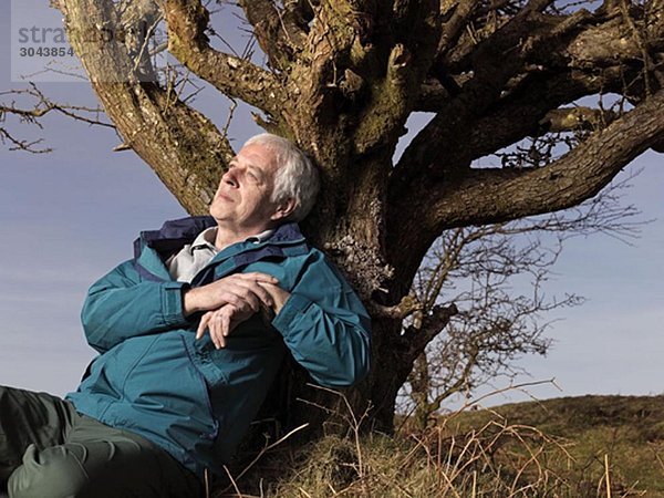 reifer Mann  der sich an einen Baum lehnt