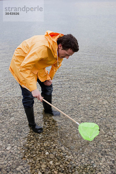 Mann im Regenmantel fischen mit Spielzeugnetz