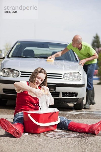 alter Mann und junges Mädchen beim Auto waschen