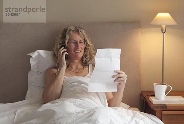 Reife Frau am Telefon im Bett