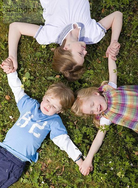 zwei Mädchen und ein Junge im Gras liegend