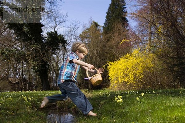 Junge springt über den Bach und hält den Korb.