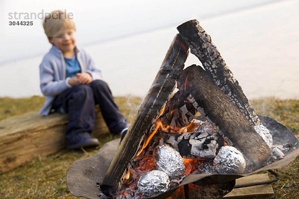 Junge schaut Kartoffeln an Grillfeuer