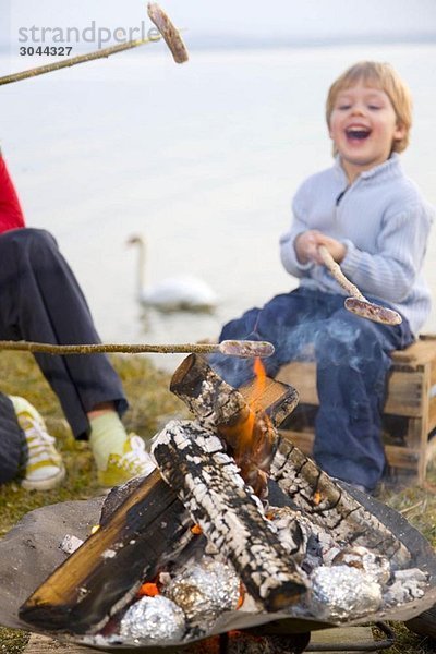 Mädchen und Junge braten Würstchen am Stiel