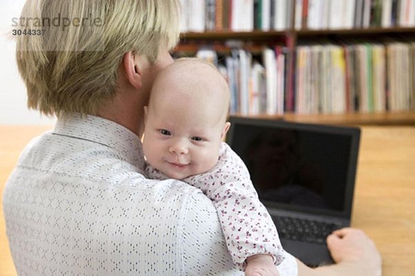 Vater arbeitet am Laptop mit Baby