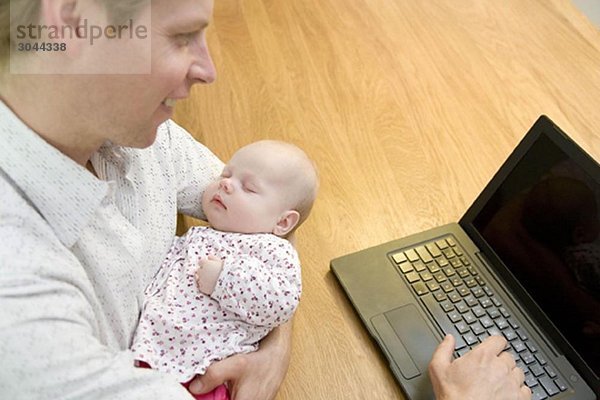 Vater arbeitet am Laptop mit Baby