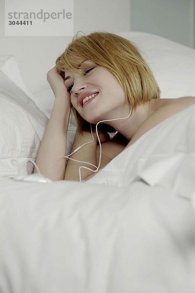 Frau liegt im Bett und trägt Kopfhörer.