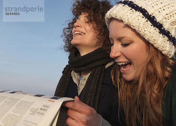 Frauen halten Zeitung  lachend