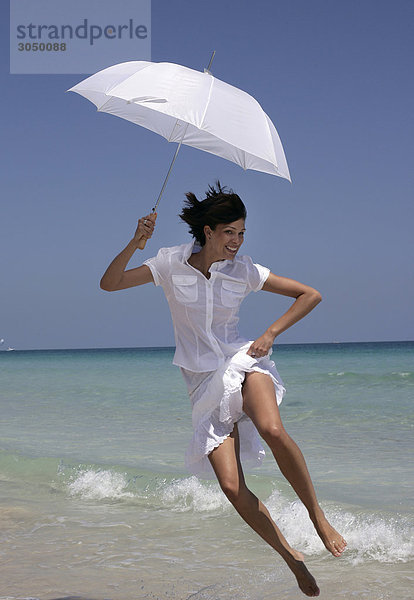Frau mit Sonnenschirm am Strand springen