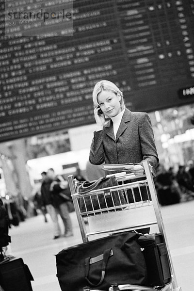 Geschäftsreisende telefonieren mit Gepäckwagen  An- und Abreisebrett im Hintergrund