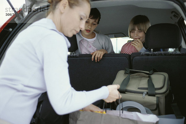 Frau organisiert Gepäck im Auto  Kinder schauen vom Rücksitz aus zu.