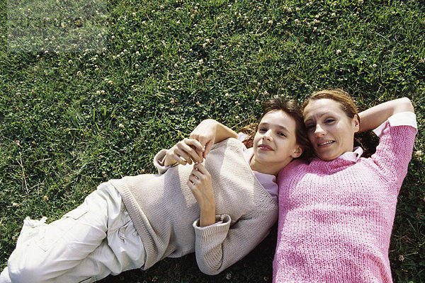 Mutter und Tochter liegen zusammen auf Gras und lächeln in die Kamera.