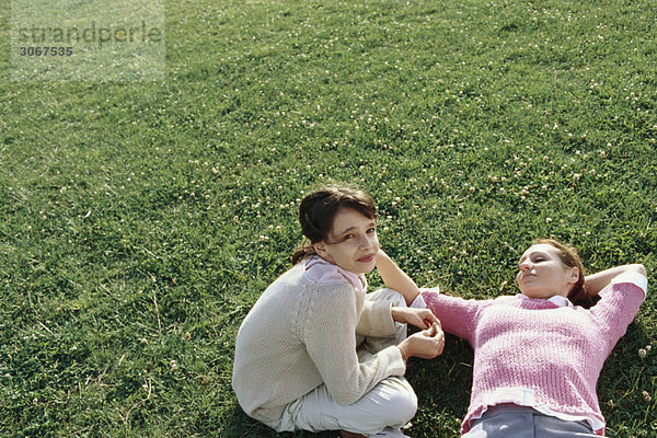 Mutter und Tochter entspannen gemeinsam auf Rasen  Mädchen schaut in die Kamera