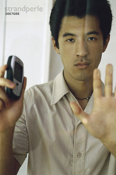Mann drückt Hand gegen Fenster  hält Handy  schaut auf Kamera