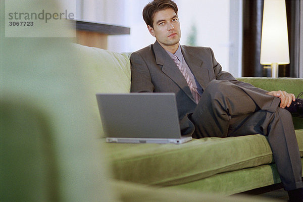 Geschäftsmann sitzt auf dem Sofa mit Laptop und schaut weg.