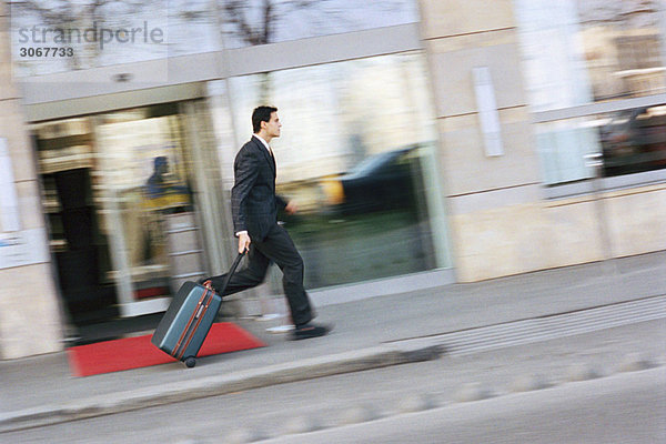 Ein Geschäftsmann rennt den Bürgersteig hinunter und zieht den Koffer hinter sich her.