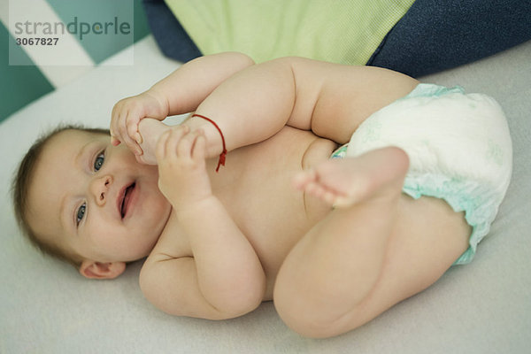 Baby auf dem Rücken liegend  mit dem Fuß spielend