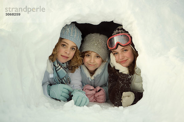 Drei junge Freunde liegen im Schneetunnel und lächeln in die Kamera.