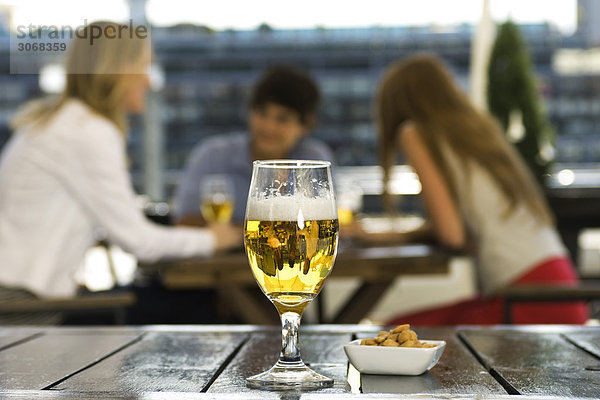 Ein Glas Bier und eine Schüssel Erdnüsse auf dem Kaffeetisch  Freunde beim Plaudern im Hintergrund