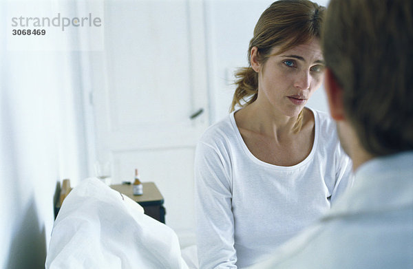 Frau auf dem Bett sitzend mit besorgter Miene  im Gespräch mit dem Arzt