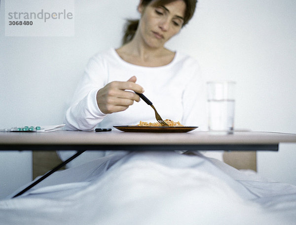 Frau sitzt im Krankenhausbett und isst Mahlzeit.