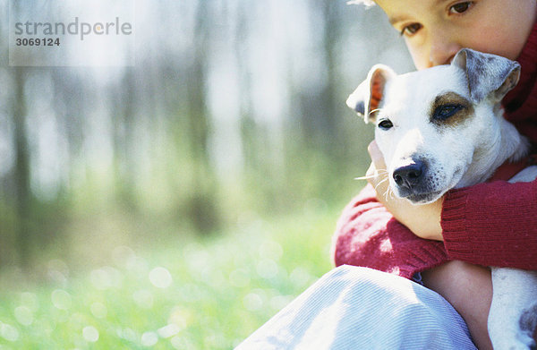Kind auf Gras sitzend mit Hund im Arm