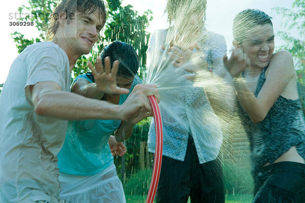 Junge Freunde beim Wasserkampf mit Gartenschlauch