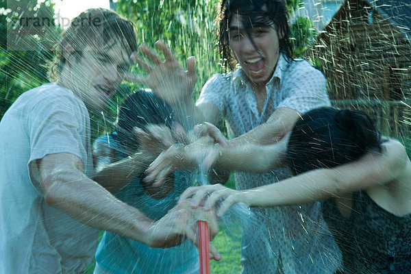 Junge Freunde beim Wasserkampf mit Gartenschlauch