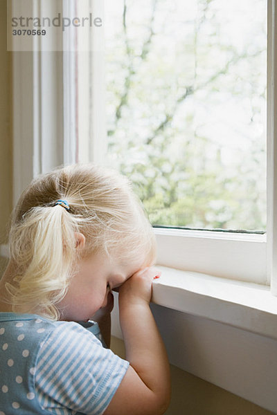 Trauriges kleines Mädchen am Fenster