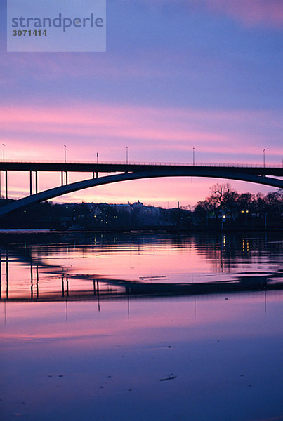 Eine Brücke über ruhigem Wasser in den Sonnenuntergang.