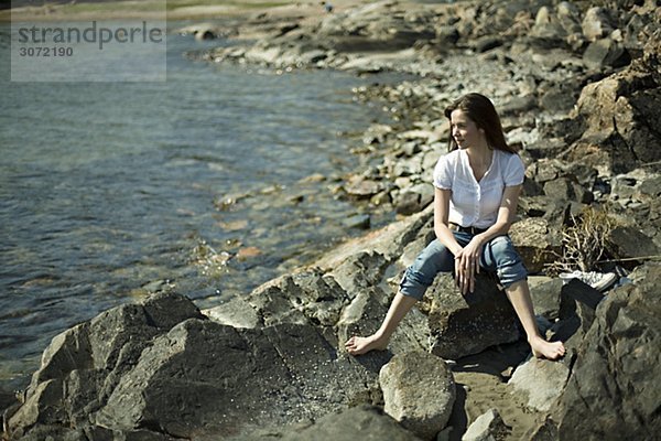 Eine junge Frau sitzend auf Klippen am Meer Ingaro Schweden