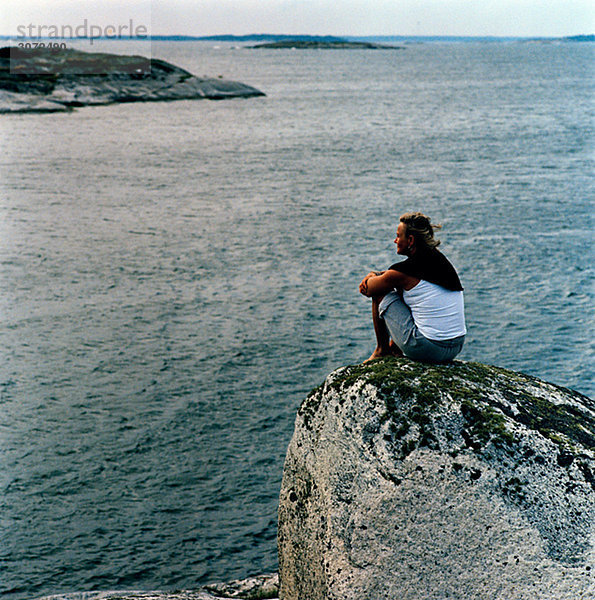 Eine Frau sitzend auf einem Felsen am Meer Schweden
