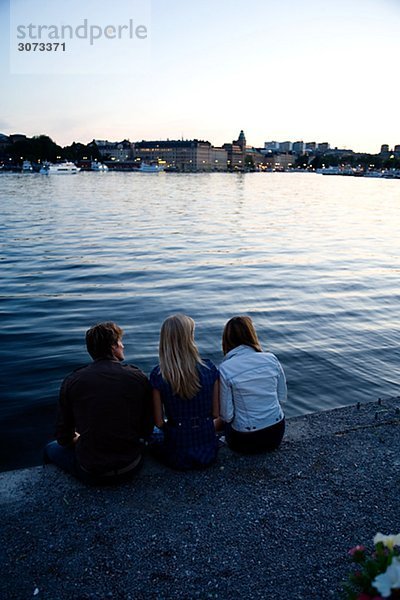 Three friends sitting on a quay-edge Stockholm Sweden.