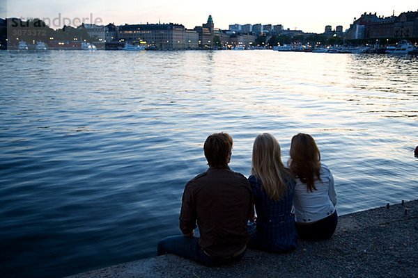 Three friends sitting on a quay-edge Stockholm Sweden.