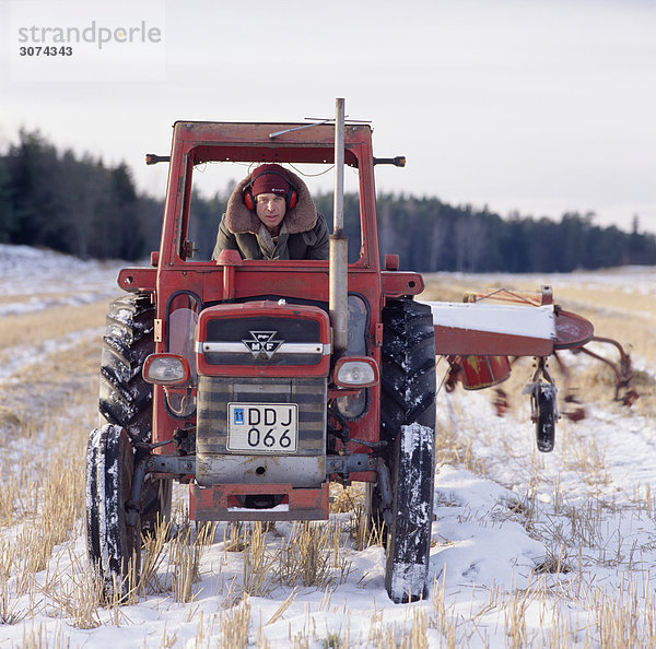 Junger Mann fahren Traktor in schneebedeckten Feld