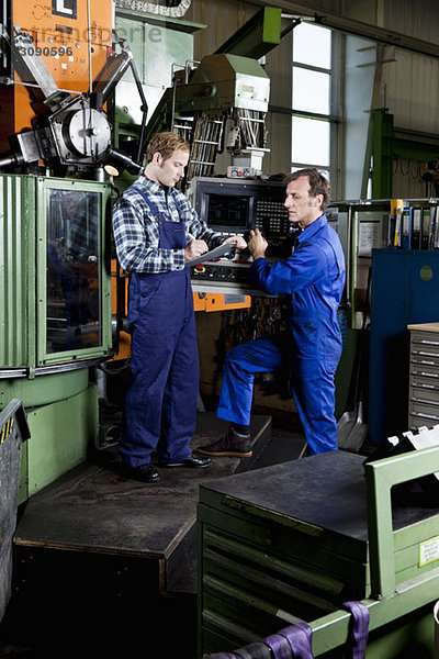 Zwei Männer in einer Metallteilefabrik beim Durchsehen eines Klemmbrettes