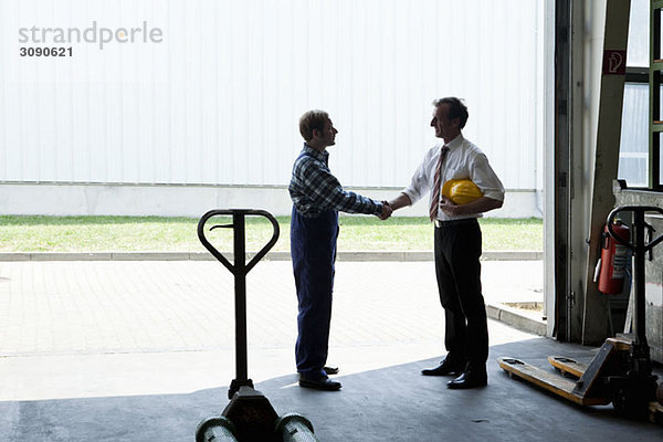 Ein Handwerker schüttelt einem Manager in einem Metallteilelager die Hand.