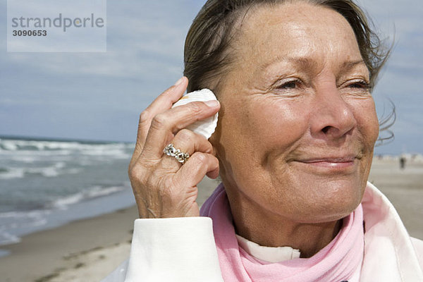 Eine ältere Frau mit einer Muschel am Ohr