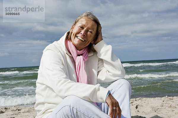 Eine ältere Frau  die am Strand sitzt.