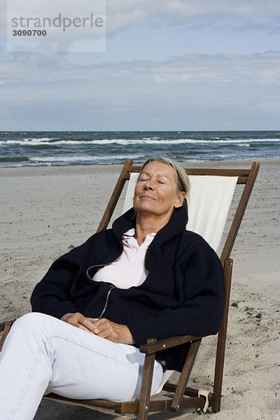 Eine ältere Frau  die in einem Liegestuhl am Strand liegt.